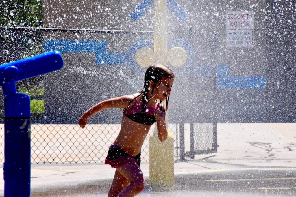 a girl in a bikini playing in a water fountain.