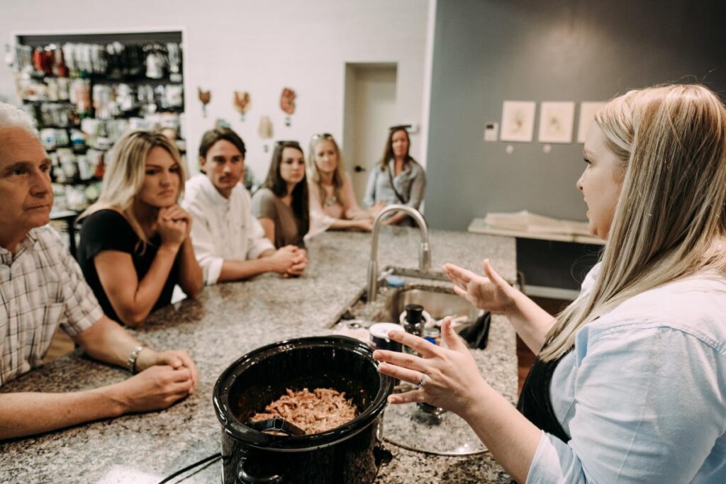 a group of people sitting around a table while a woman talks to them.